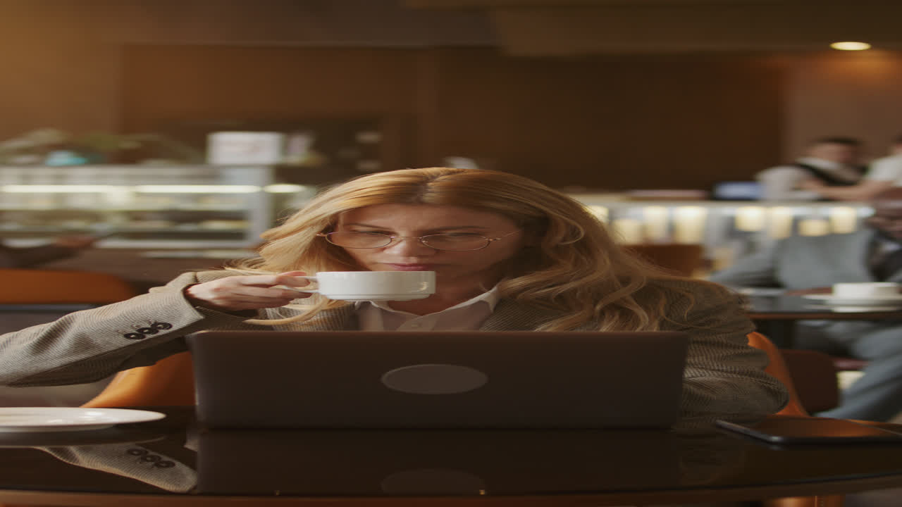 Businesswoman Working Remotely on Laptop and Drinking Coffee in Hotel Lounge