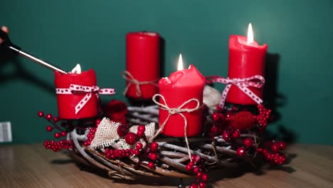 hands of mother and child, holding a lighter, lighting candles on modern christmas wreath with four red candles on wooden surface with green background, holiday interior design