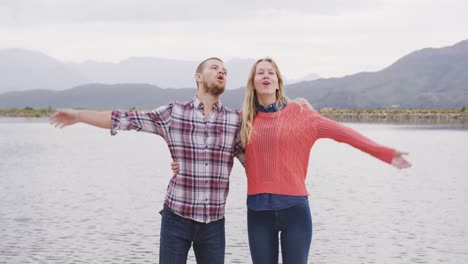 caucasian couple having a good time on a trip to the mountains, embracing and raising their hands