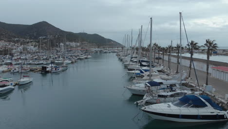 drone-captures-yachts-docked-near-coastal-town-with-mountain-backdrop