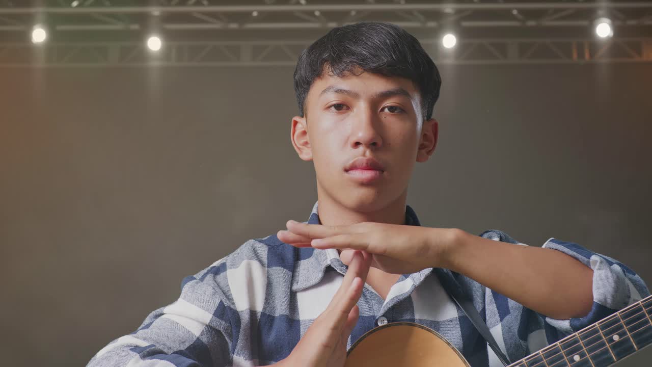 기타를 들고 있는 아시아 십대가 무대 위에 손을 고 타임아웃을 하고 있다.