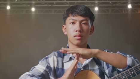 primer plano de un adolescente asiático con una guitarra haciendo un gesto de tiempo con las manos en el escenario