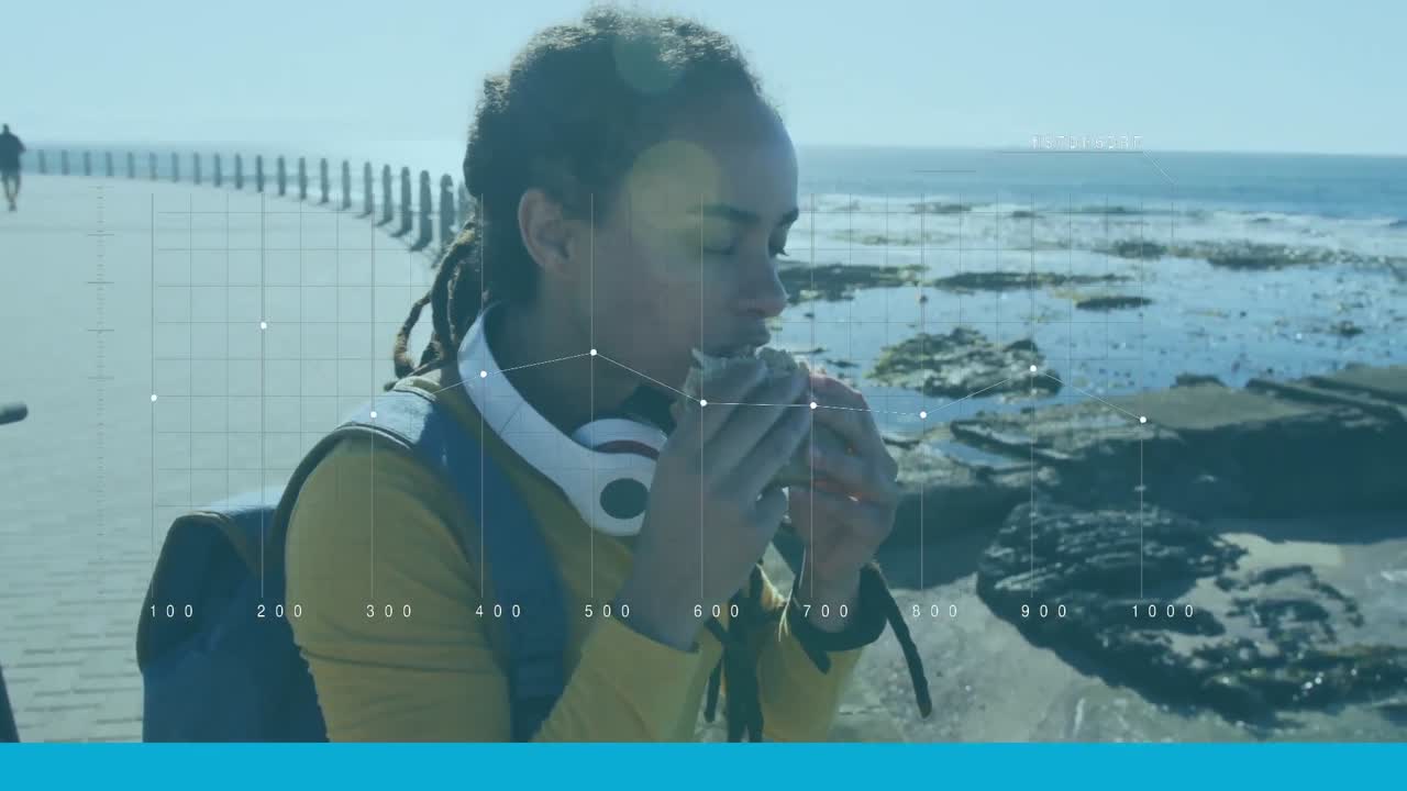 procesamiento de datos estadísticos contra una mujer afroamericana que come un bocadillo en el paseo marítimo