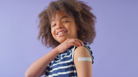 Studio-Shot-Of-Young-Boy-With-Sticking-Plaster-On-Arm-Against-Purple-Background