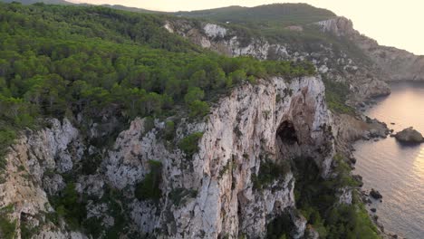 Hikers-rest-on-a-rocky-cliff-among-trees-with-a-view-of-the-green-landscape-during-sunset-in-ibiza