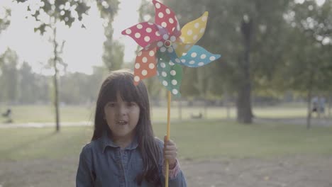 chica latina sosteniendo un abanico de papel, parada en el parque y sonriendo a la cámara