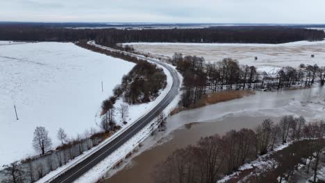a winding, asphalted country road stretches through meadows and forests in the wintertime. baltic states europe.