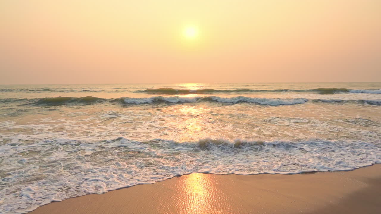 Slow motion scene of a romantic sunset over the peaceful ocean with waves reaching wet sand