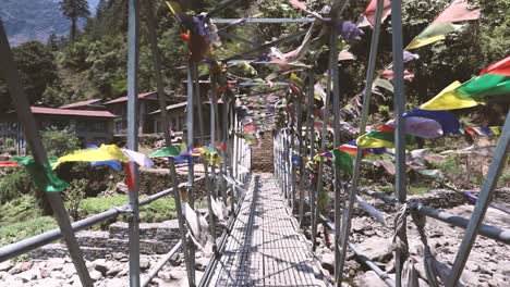 un puente peatonal de metal en nepal con banderas de oración ondeando en el viento