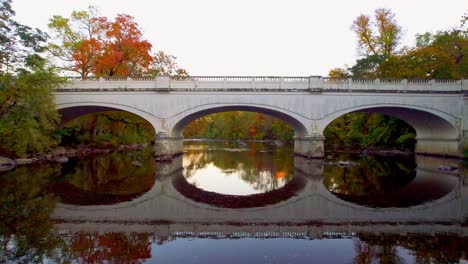 drone flyover and tilt down on river bridge during autumn fall