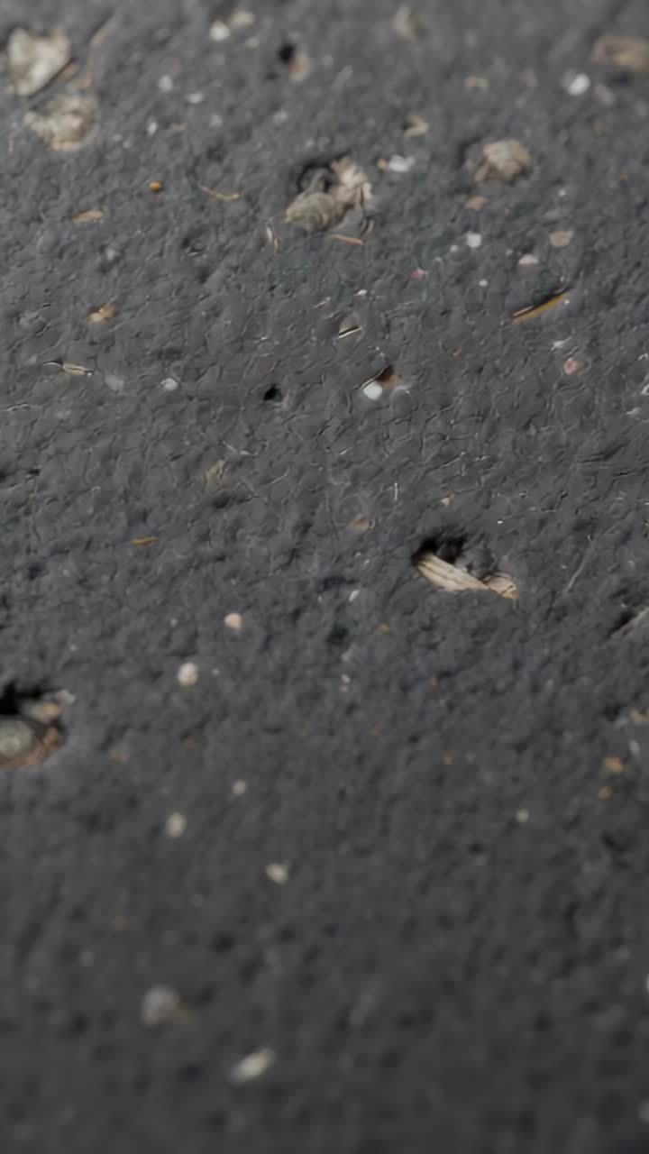 Vertical video: Panning handheld cam scanning dark coarse surface closeup, showing pits and chips