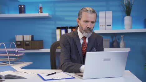 mature businessman working on laptop at table in office.