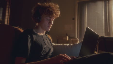 focused young man in headphones typing on laptop at home