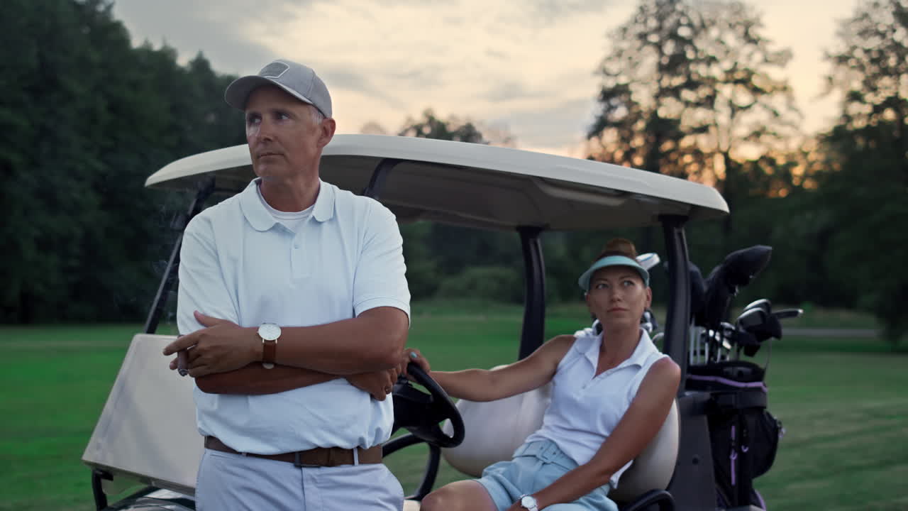 Wealthy golf players resting at golf cart. Sport couple enjoy summer weekend.