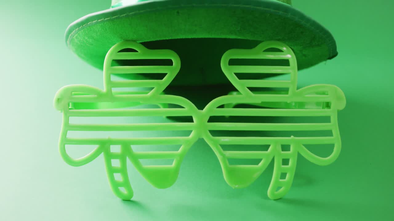Video of st patrick's shamrock leaf glasses and hat with copy space on green to white background