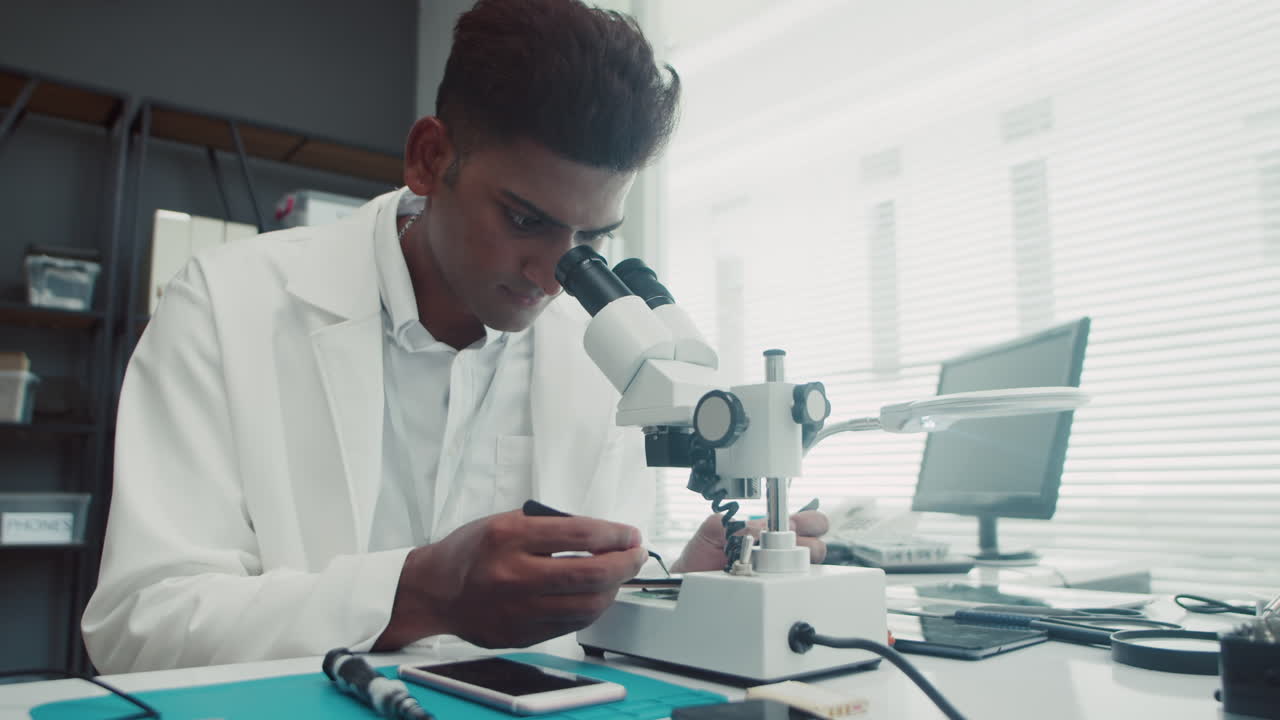 Male Specialist Using Microscope when Fixing Broken Detail in Phone