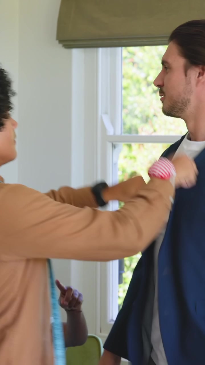 Video verticale: Sarto che si muove con il metro in una stanza, provando un blazer blu navy su un cliente con chignon per la vestibilità.