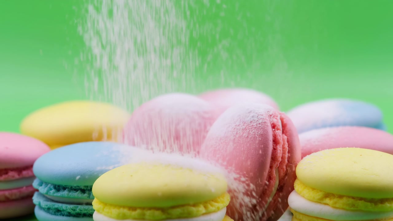 Macarons colorati spolverati di zucchero, sfondo verde vibrante, pioggia di zucchero al rallentatore su macarons pastello impilati