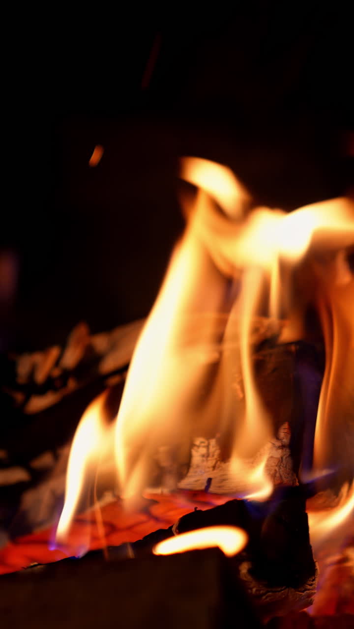 Orange flame in fireplace on black background. Wooden logs in fire flame. Warm cosy fire burning in fireplace. Close-up. Vertical video