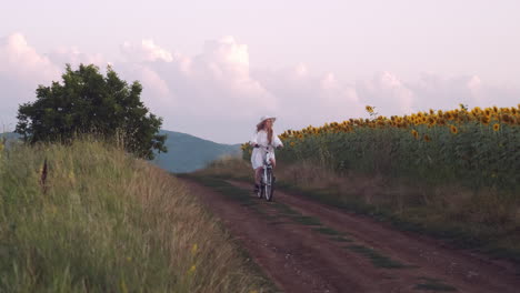 girl in white dress rides bike in rural countryside at golden hour slow mo