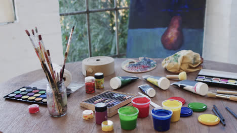 Close-up-of-paints-and-brushes-on-table-in-studio,-slow-motion