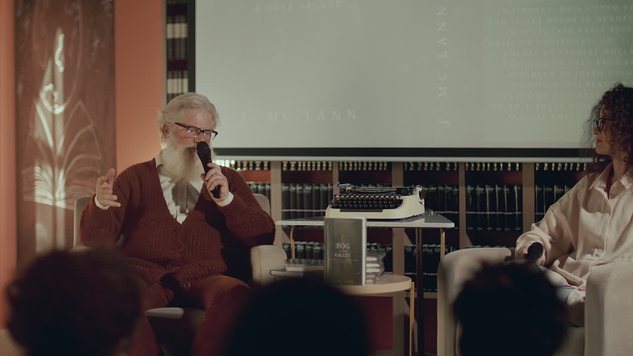 노인 작가 가 문학 행사 에서 청중 에게 책 에 대해 이야기 하고 있다