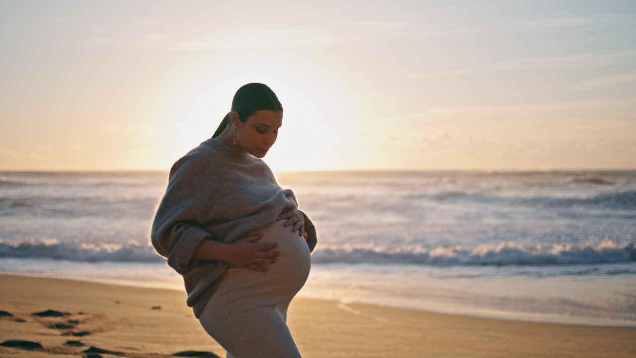 Expectant mother posing sunset standing beach caressing belly. Pregnant woman