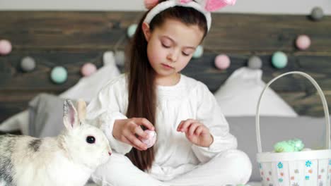 girl playing with rabbit and easter eggs on the bed