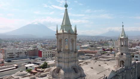 Disfrute-De-Un-Impresionante-Primer-Plano-De-Una-De-Las-Torres-De-La-Catedral-De-Arequipa,-Con-El-Majestuoso-Volcán-Misti-Y-El-Imponente-Chachani-Al-Fondo,-En-Un-Día-Tranquilo-Rodeado-De-Nubes