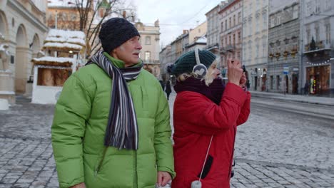 Senior-old-couple-tourists-grandmother-grandfather-walking-in-city,-taking-photo-pictures-on-camera