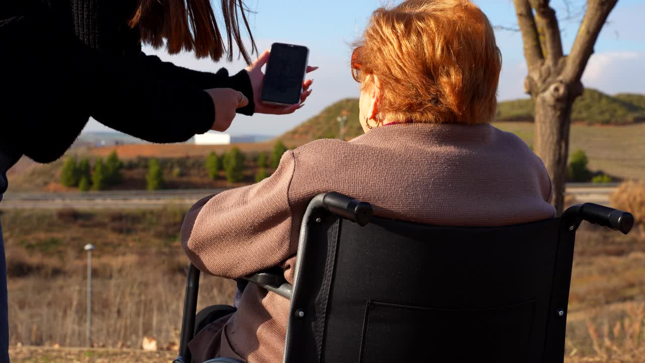Surprised grandmother zooming on smartphone in park with granddaughter