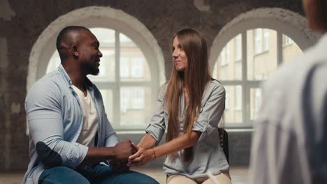 happy couple, a fit man with black skin in a blue shirt and a blonde girl are talking with a psychologist. personal conversation and therapy with a psychologist in a brick building