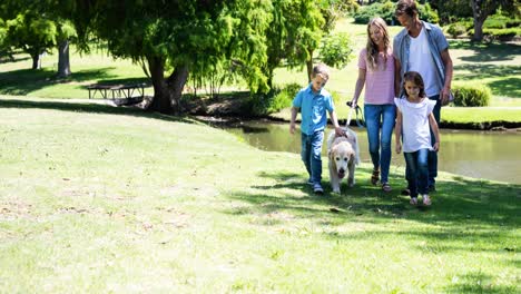 Felices-Padres-Caucásicos,-Hijo-E-Hija-Caminando-Con-Un-Perro-Mascota-En-El-Parque