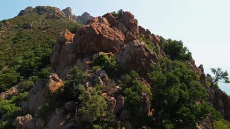 Schroffer-Roter-Felsberg-Mit-Grüner-Mediterraner-Vegetation-An-Einem-Sonnigen-Tag-In-Sardinien,-Italien---Luftdrohne-Aus-Nächster-Nähe