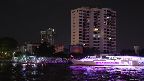 a brightly lit boat cruises along a river at night.