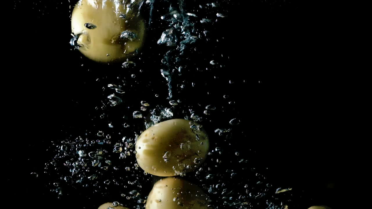 papas caídas en agua sobre fondo negro, cámara lenta de cerca