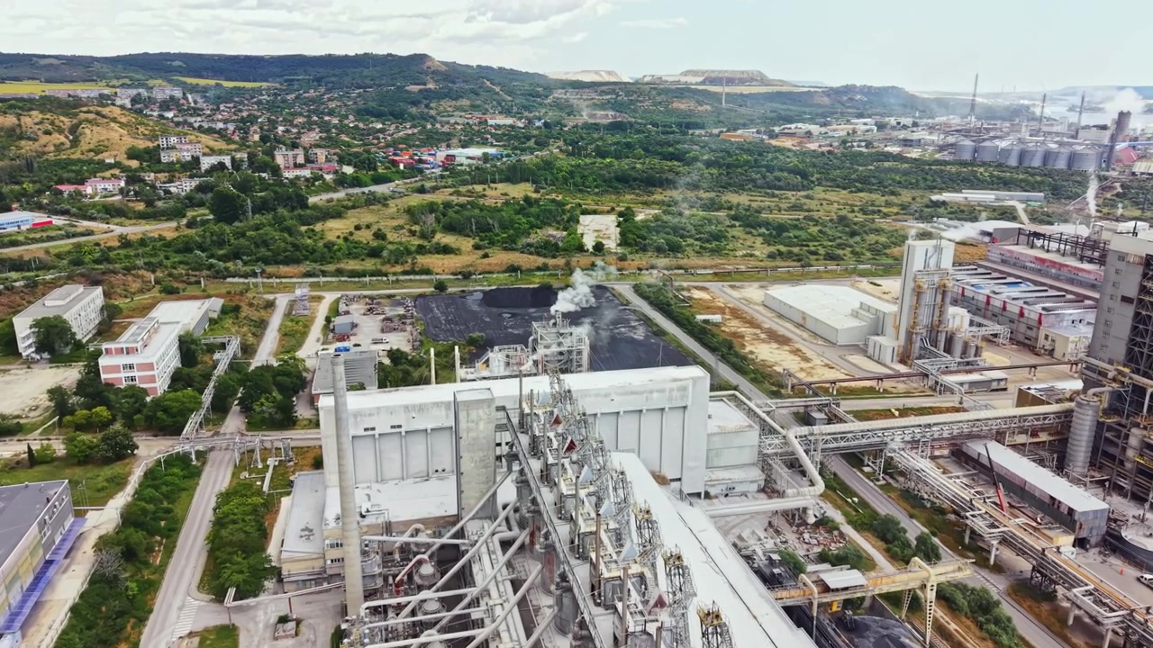 Vista de una zona industrial con fábricas, maquinaria y montañas al fondo durante el día en un día despejado.