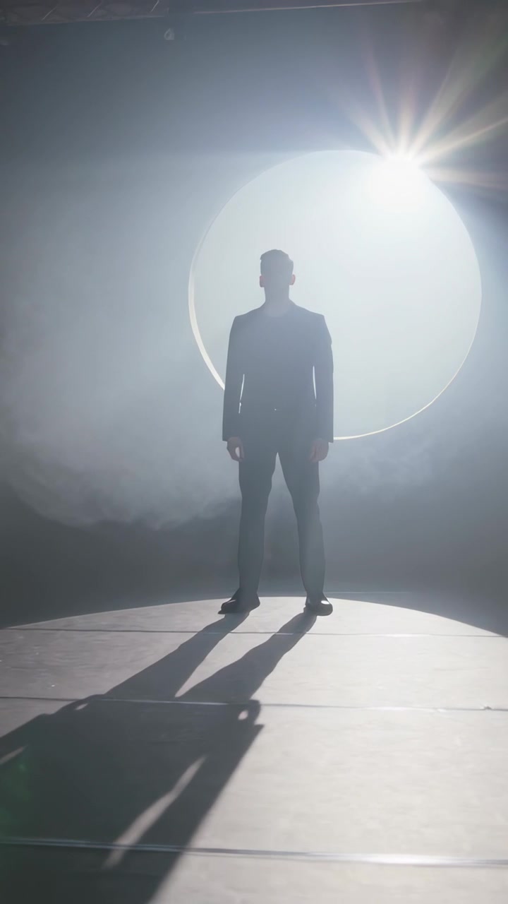 Video verticale: Uomo in piedi in abito, rivolto in avanti sul palco, con un alone cangiante che crea una silhouette
