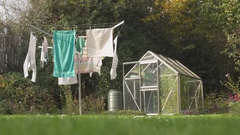 a foldable outdoor clothesline with clean clothes hangs to dry next to a small greenhouse