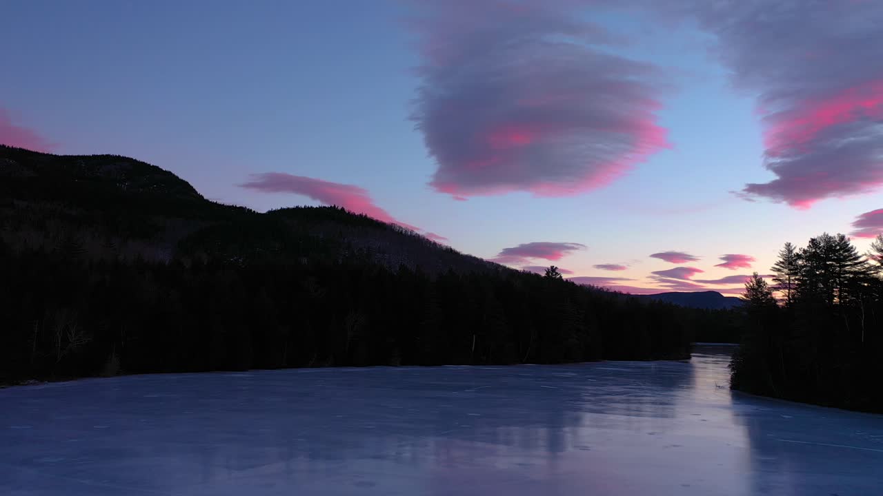 Riprese aeree che si alzano sopra la superficie di uno stagno ghiacciato volando verso nuvole color zucchero filato rosa e viola.