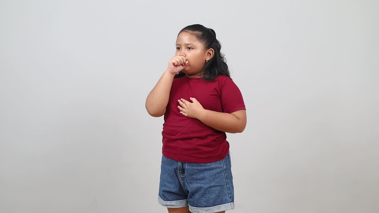 Adorabile bambina asiatica che indossa abiti casual, si sente poco bene e tossisce come sintomo di raffreddore o bronchite