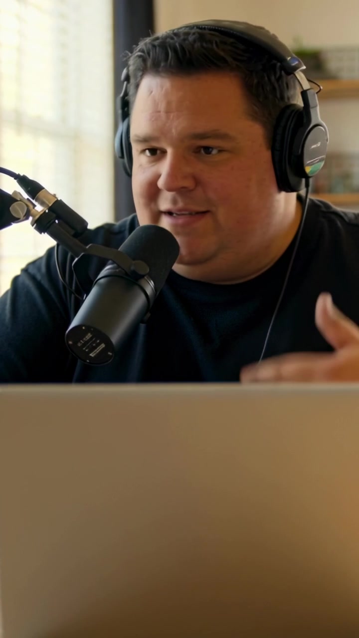 Vertikal video: Mand læser på bærbar computer i sort T-shirt, læner sig ind i mikrofonen derhjemme, er vært for et show og gestikulerer