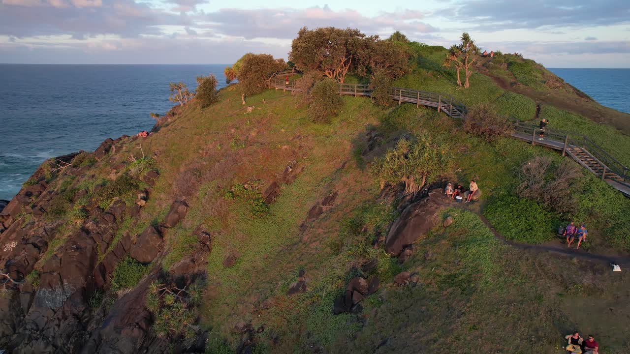 People Sit On The Edge Enjoying The Sunset View Of Norries Headland At Cabarita Beach On The Tweed Coast, NSW Australia. Aerial Pullback Shot