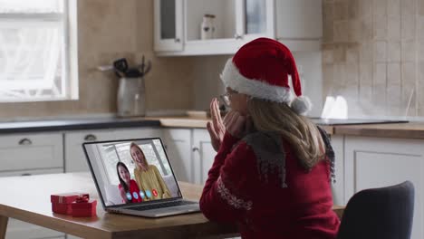 Kaukasische-Frau-Mit-Weihnachtsmannmütze-Winkt-Und-Nutzt-Laptop-Während-Eines-Videoanrufs-Mit-Zwei-Frauen-Während-Der-Weihnachtszeit