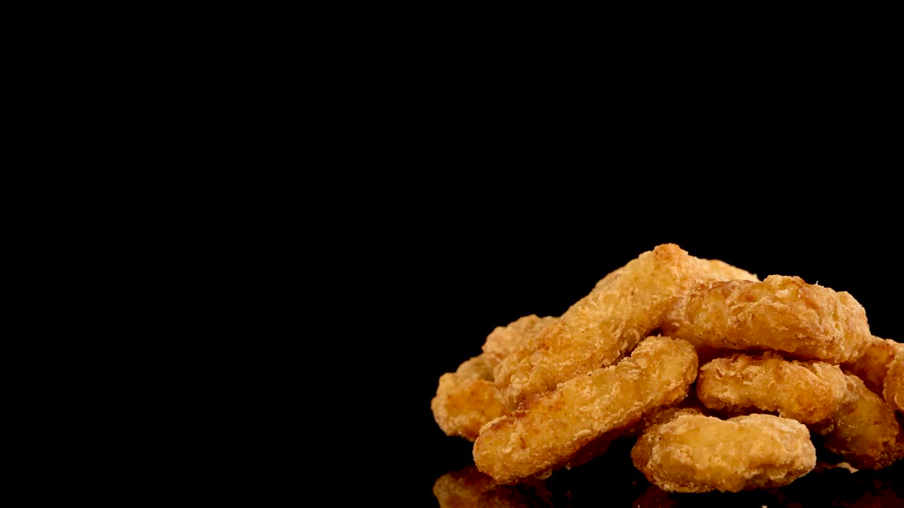 Golden, crumbed spicy chicken nuggets rotate in slow motion under studio lighting, isolated on a black background with copy space and reflective surface