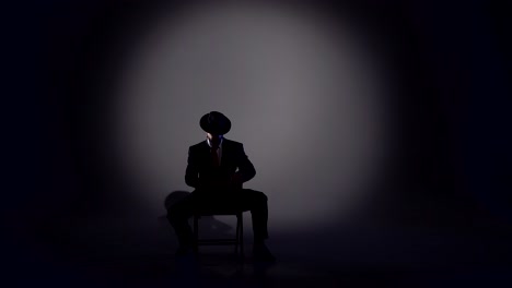 a person in a suit and hat silhouetted in a spotlight on a dark stage