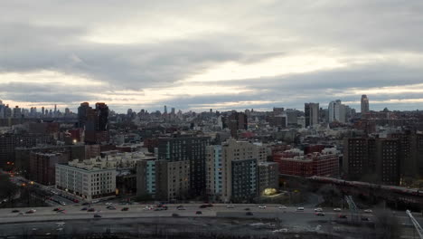 Aerial-view-rising-over-traffic-on-the-Harlem-river-drive-and-a-train,-in-cloudy-NY,-USA