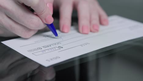 business woman hand signs and filling bank check for one thousand 1000 dollars