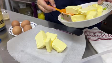 measuring the precise quantity of butter for baking recipe, placing it on top of the kitchen scale with baking paper using a spatula, close up shot