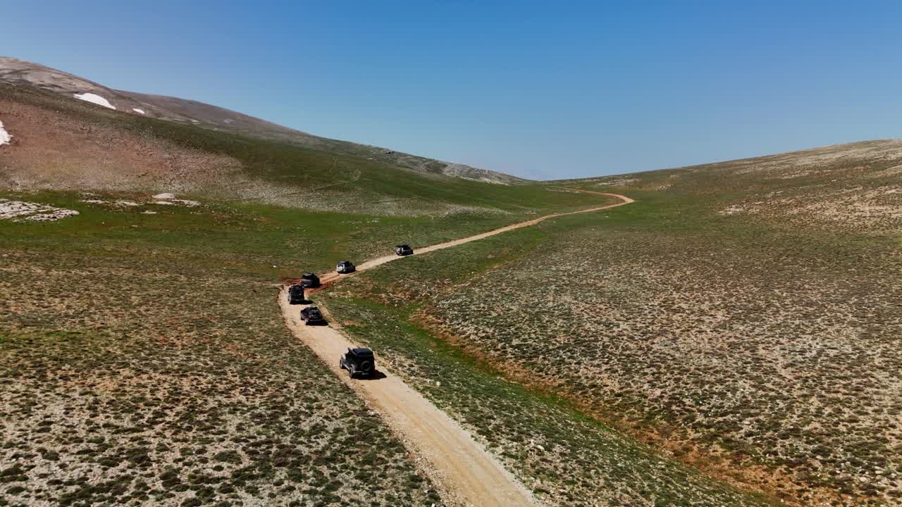 Off-road vehicles traverse a scenic mountain dirt road in clear weather